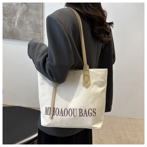 Side view of large canvas tote bag with brown straps worn over a grey blazer
