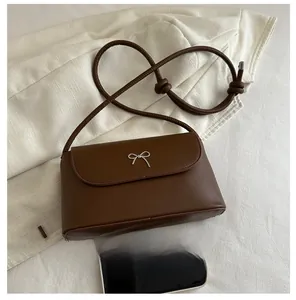 Détail du petit sac bandoulière marron avec nœud argenté et téléphone pour comparer la taille