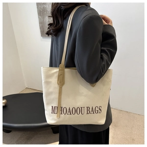 Close-up of the beige canvas tote bag with brown leather handles worn on shoulder