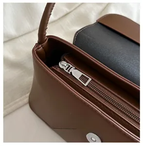 Détail macro du zip en métal argenté sur le sac à main en cuir marron foncé au fini mat