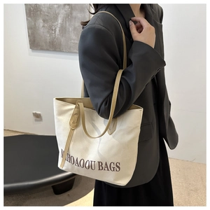 Detail of beige canvas tote bag featuring brown leather straps and NIHOAOOU typography