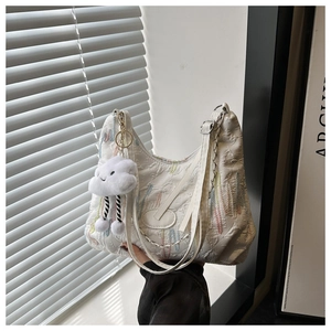 Close-up of white textured tote bag with colorful embroidery and plush cloud charm