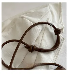 Détail d'une poignée de sac à main en cuir marron avec nœud décoratif et boucle argentée