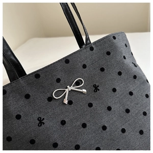 Close-up of dark grey tote bag featuring black flocked dots and silver bow charm