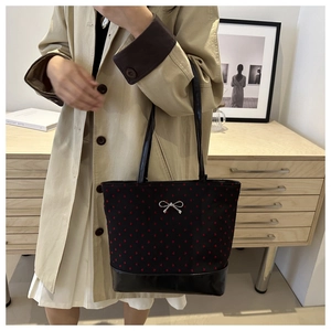 Detail of black tote bag with red heart pattern and silver bow on beige coat model