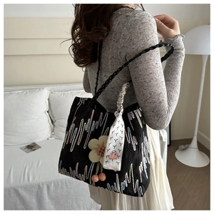 Detailed close-up of a black fabric tote bag with colorful embroidery and floral pendant