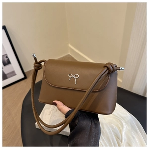 Détail d'un sac bandoulière en cuir marron foncé avec un nœud papillon argenté