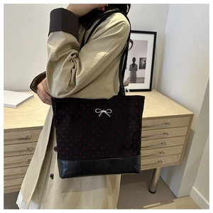 Detail of a black tote bag with red heart pattern and silver bow on female shoulder