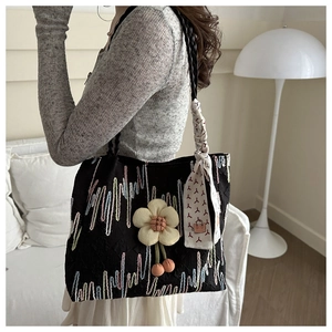 Detail of black embroidered tote bag with flower charm and silk scarf handle on model