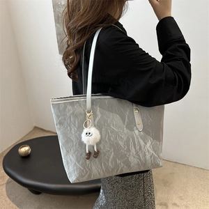 Silver-grey pleated tote bag with plush monster charm worn by a model in a minimalist setting