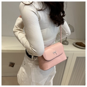 Detailed side view of pink shoulder bag with silver bow ornament worn by a model
