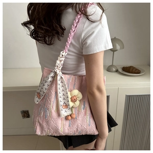 Detail of pink tote bag with textured fabric, woven strap, and floral scarf accessory