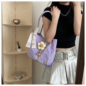 Close-up of purple quilted tote bag with silk scarf and floral charm on a wooden shelf