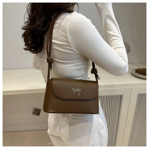 Detail of a dark brown leather shoulder bag featuring a silver metal bow buckle and knot strap