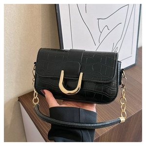 Detail of black crocodile texture handbag with large golden U-shaped buckle and metal chain