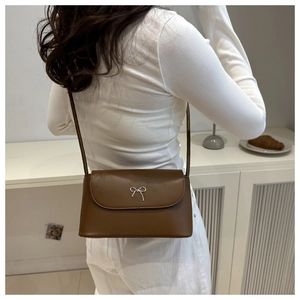 Detailed close-up of brown leather crossbody bag with silver bow hardware and fine texture