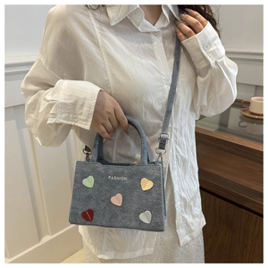 Detail of grey handbag with colored heart patches and adjustable shoulder strap