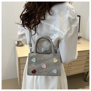 Close-up of gray suede tote bag with colorful heart patches and silver fashion text