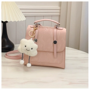 Detail of a light pink square handbag with decorative straps and a smiling cloud charm