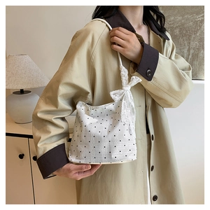 Détail d'un sac seau blanc à pois avec nœud en dentelle porté par un mannequin en trench-coat