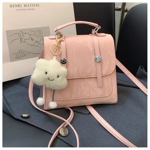 Detailed view of pink glossy PU handbag with a white fluffy cloud charm on grey fabric