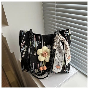 Detail of black canvas tote with wave embroidery, woven handle, and floral charm