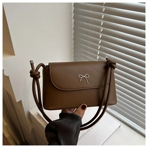 Detail of a brown leather crossbody bag featuring a silver metal bow buckle and knotted strap
