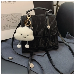 Detail view of black glossy pleated texture bag with a cute white plush cloud charm