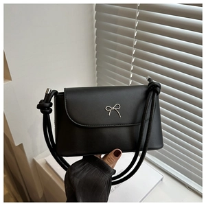Detail of a black leather crossbody bag with a silver metal bow accent and knotted strap