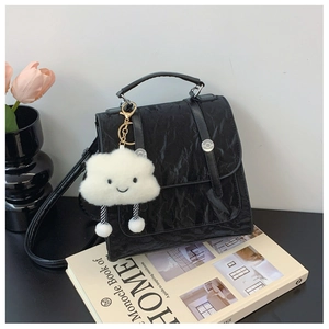 Detail view of black pleated texture handbag with white plush cloud charm on a desk