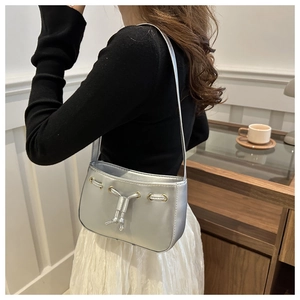 Detail of silver metallic drawstring shoulder bag shown on model with gold hardware accents