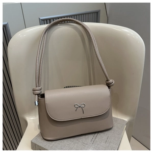Detail of light beige faux leather bag with silver bow accent on a textured book surface