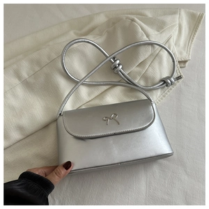 Close-up of silver metallic square bag featuring bow detail and knotted shoulder strap