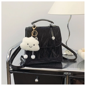Close-up of black pleated texture backpack with a plush white cloud charm on metal shelf