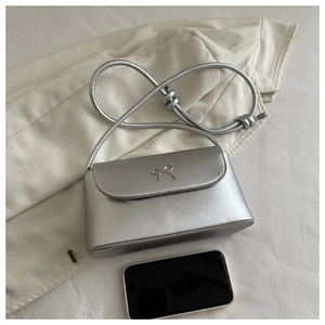 Close-up of silver mini crossbody bag with metal bow detail and size comparison to phone