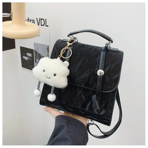 Detail of black pleated faux leather bag featuring a flap closure and cloud plush charm