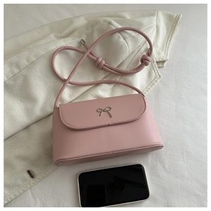 Detailed view of pink shoulder bag with metal bow and smartphone for size reference