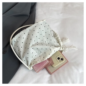 Détails du sac seau blanc à pois avec dentelle contenant un téléphone et du maquillage