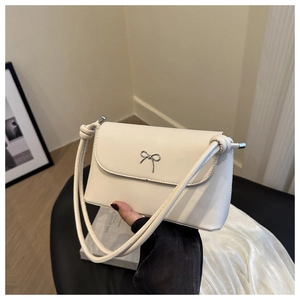 Détail d'un sac à rabat blanc crème avec boucle noeud en métal argenté et bandoulière nouée