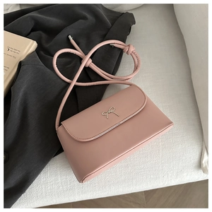 Close-up of pink leather handbag featuring a golden bow buckle and knotted strap details