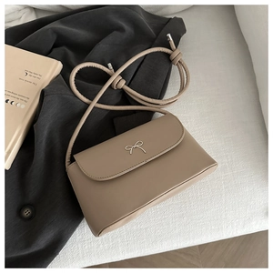 Close-up of khaki leather shoulder bag featuring a silver metal bow clasp on the flap