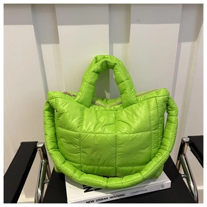 Close-up of bright green quilted puffer tote bag with wide padded shoulder strap on a chair