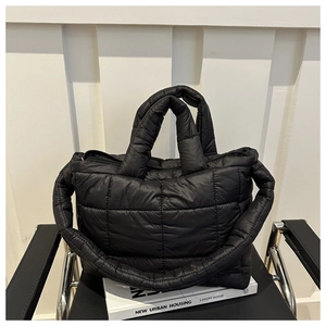 Detail view of black quilted down tote bag with dual straps on book and chair