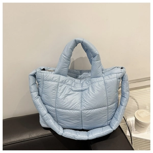 Close-up of light blue quilted nylon tote bag with padded handle and zipper on leather sofa