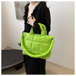 Detail of a bright green quilted puffer tote bag with wide shoulder strap on a model