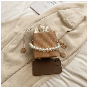 Mini brown bucket bag with pearl handle and striped texture shown next to a phone
