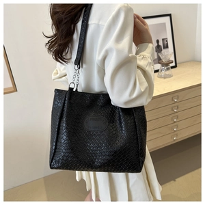 Close-up of black woven tote bag featuring metal chain strap and logo on model's shoulder
