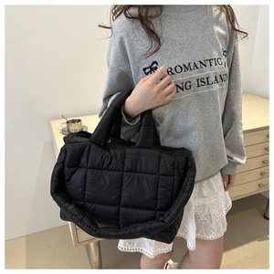 Close-up of black quilted puffer tote bag with square stitching and wide shoulder strap