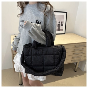 Close-up of black quilted puffer tote bag featuring wide shoulder straps in a home setting