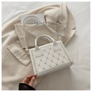 Detail of white quilted crossbody bag with golden heart embroidery and top handle